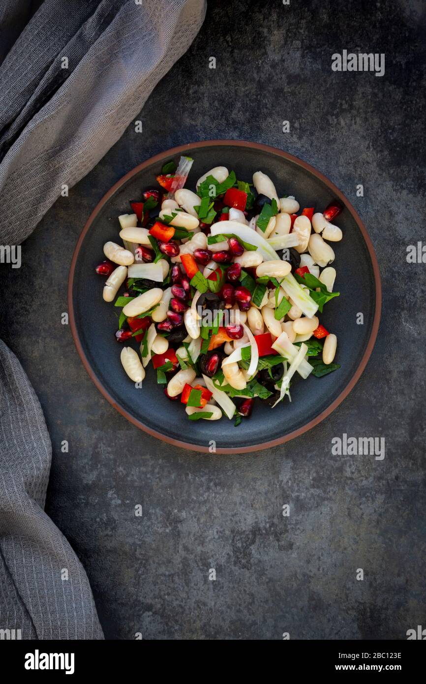 Assiette de salade de haricots de cannellini avec fenouil, poivron, olives noires, graines de grenade, menthe et persil Banque D'Images