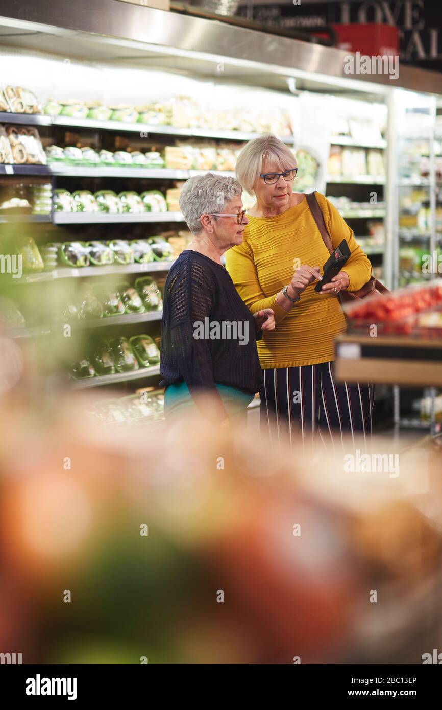 Femmes âgées avec magasin d'épicerie de téléphone intelligent dans le supermarché Banque D'Images