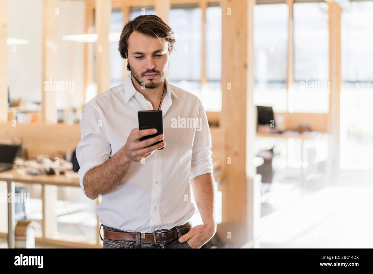 Homme d'affaires utilisant le téléphone portable dans un bureau en bois à plan ouvert Banque D'Images