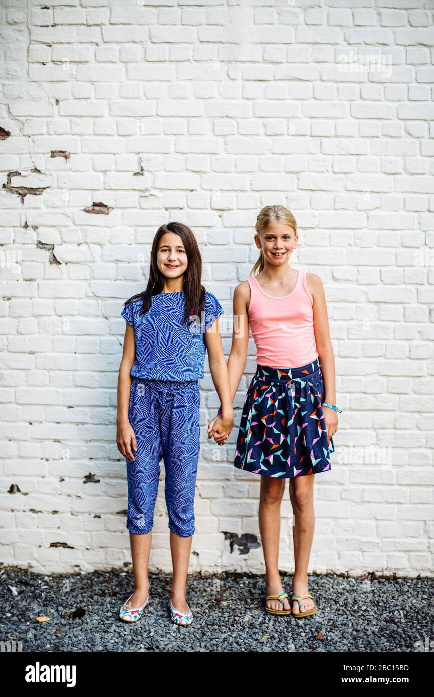 Portrait de deux filles souriantes debout à la main sur un mur Banque D'Images