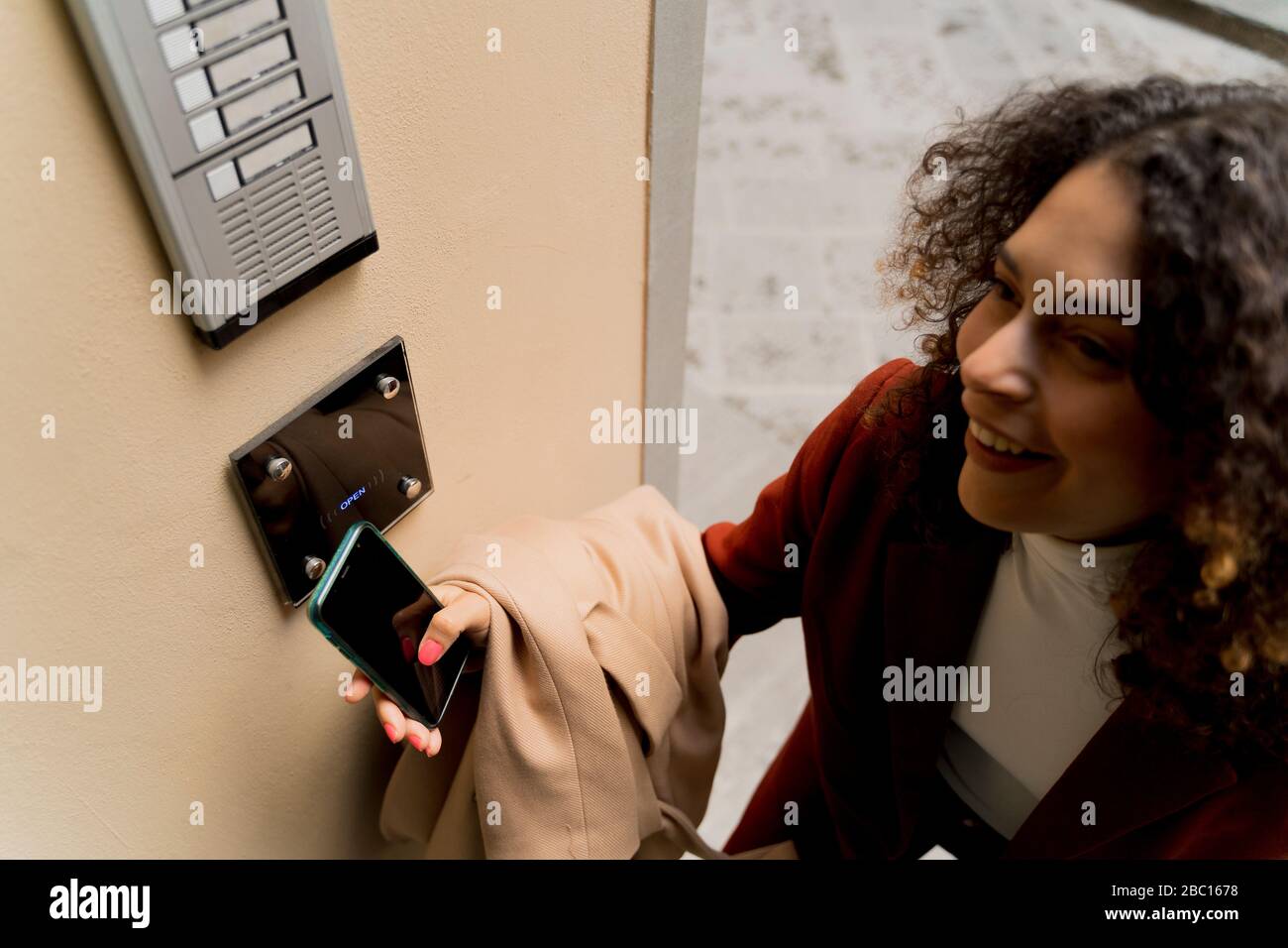 Femme souriante ouvrant la porte avec smartphone Banque D'Images