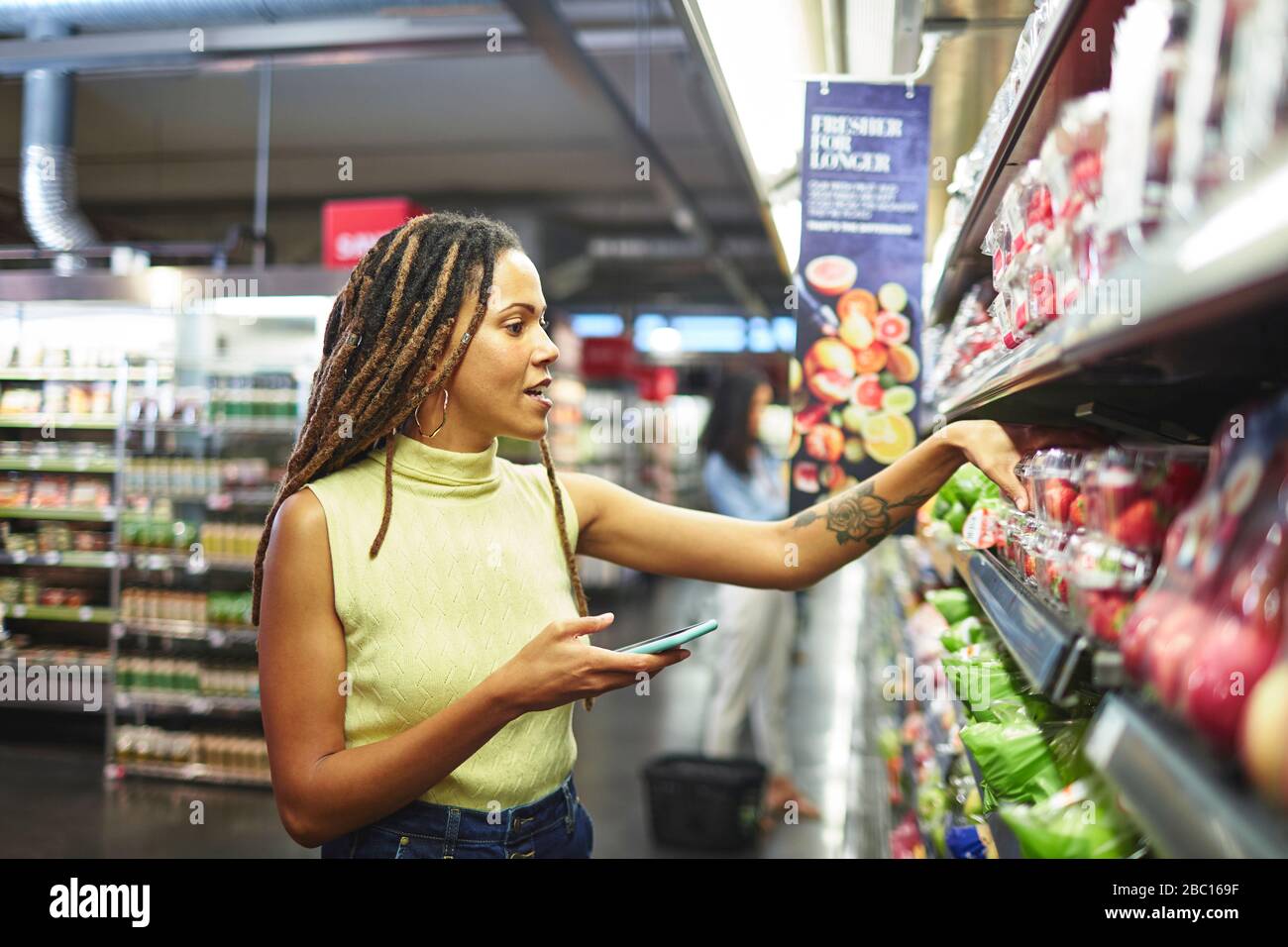 Femme avec un magasin d'alimentation de téléphone intelligent dans un supermarché Banque D'Images