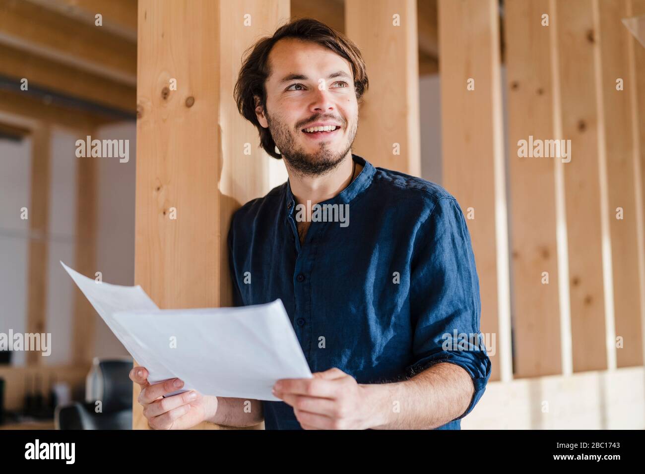Homme d'affaires souriant tenant des documents dans un bureau en bois à plan ouvert Banque D'Images
