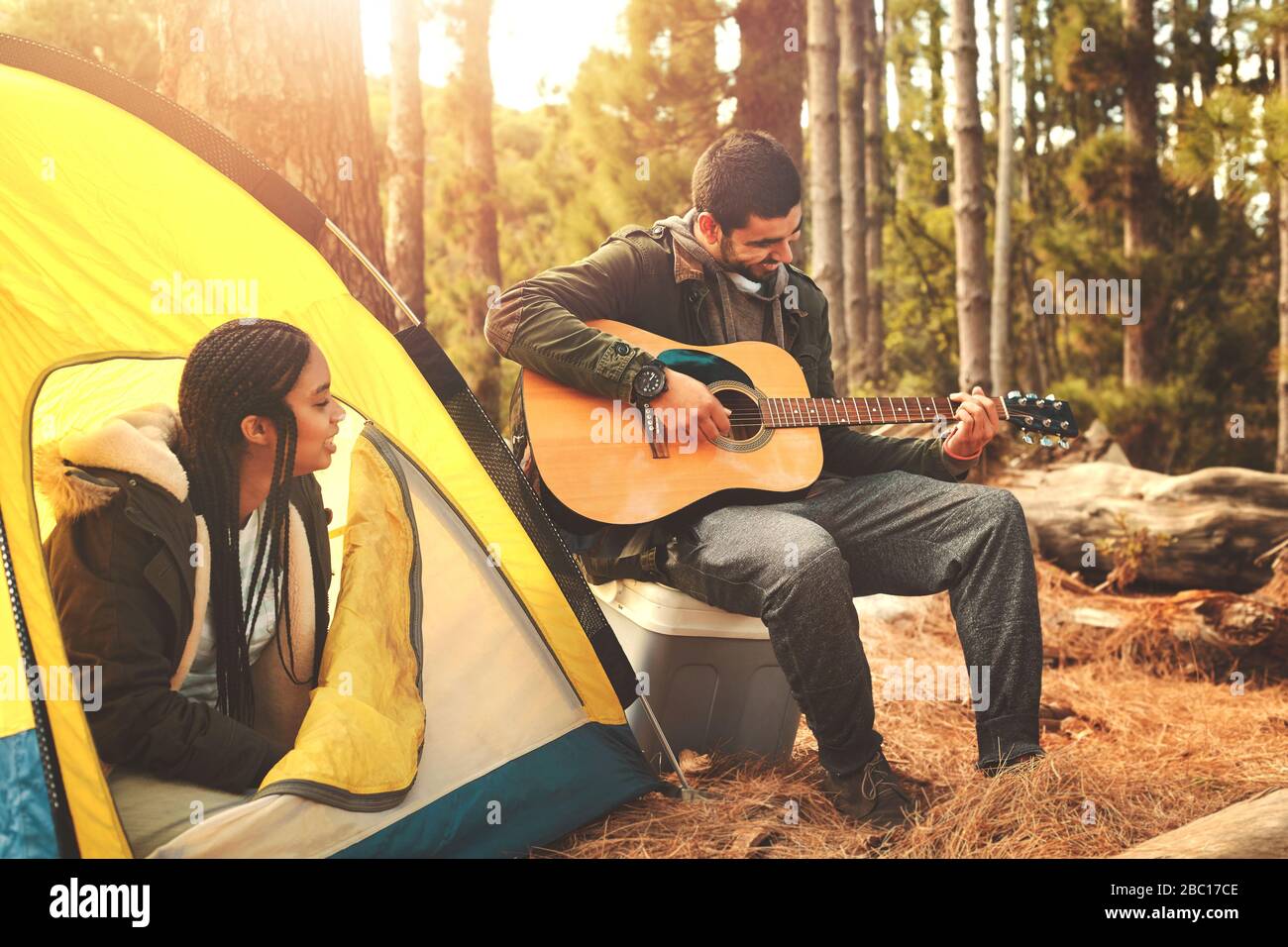 Jeune couple jouant de la guitare à la tente au camping dans les bois Banque D'Images