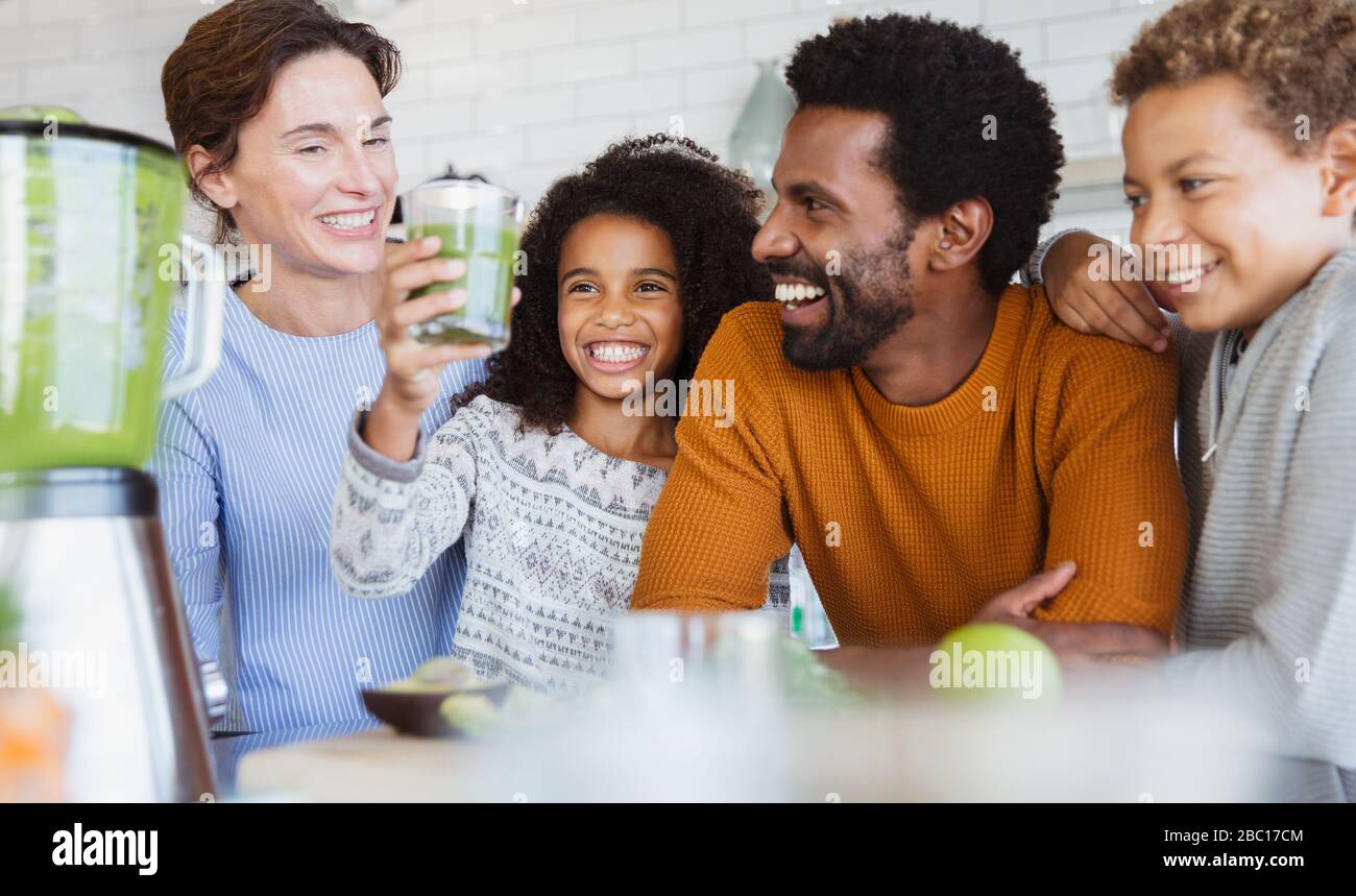 Famille multi-ethnique souriante buvant un smoothie vert sain dans la cuisine Banque D'Images