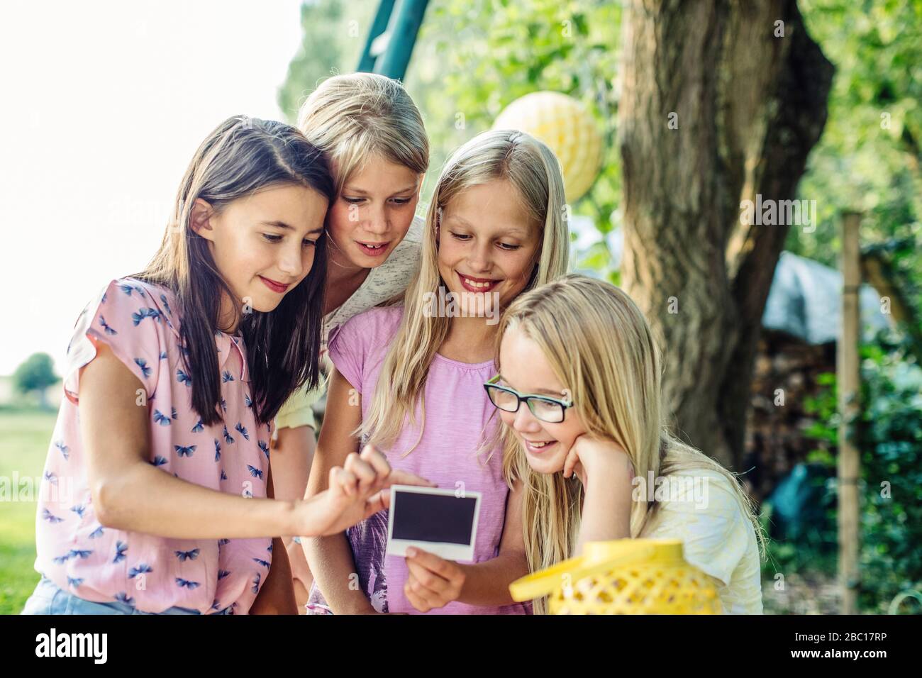 Des filles heureuses regardant la photo instantanée sur une fête d'anniversaire en plein air Banque D'Images