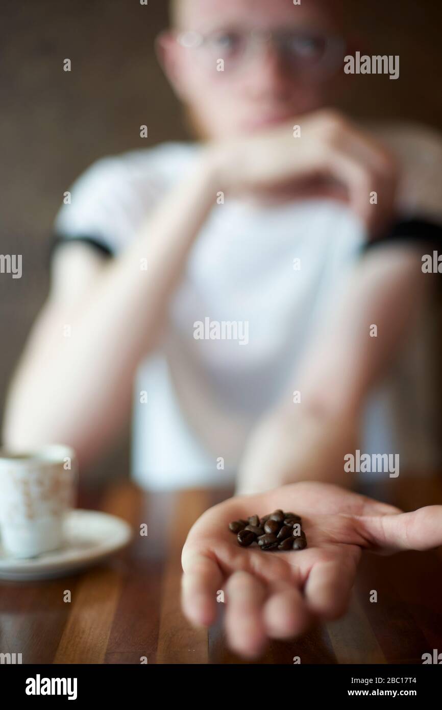 Albino homme dans une cafétéria tenant des grains de café dans une main Banque D'Images