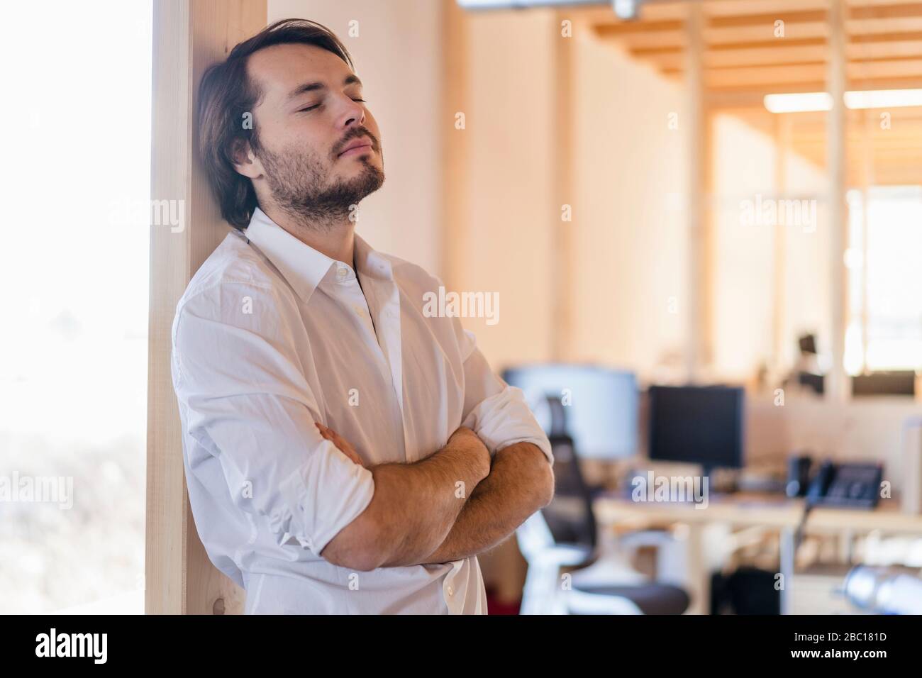 Homme d'affaires avec des yeux fermés penchant contre le faisceau dans un bureau en bois à plan ouvert Banque D'Images