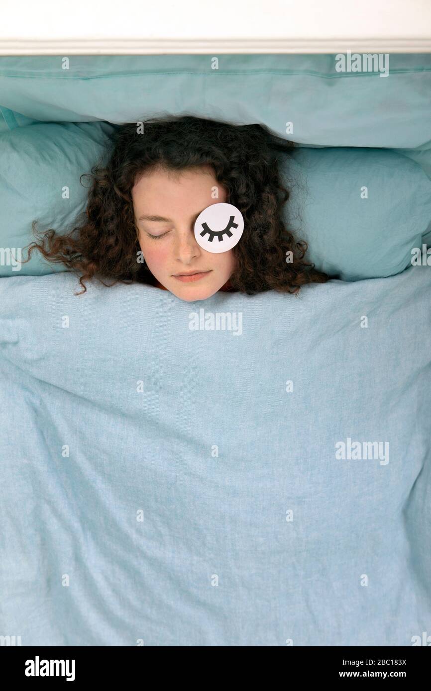 Portrait de la jeune femme endormie posée dans le lit avec masque en papier Banque D'Images