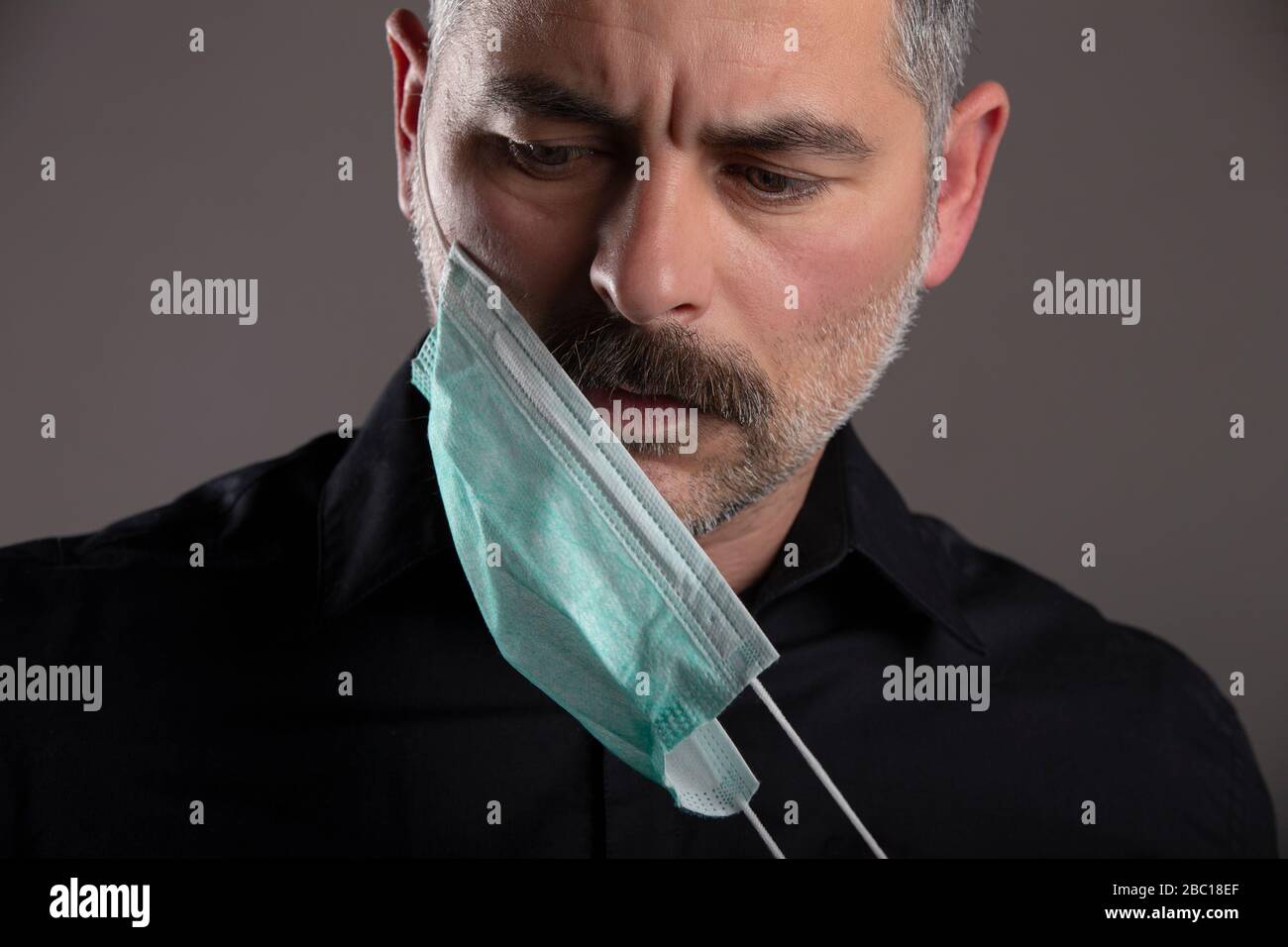 Portrait de l'homme avec masque de protection médicale sur fond gris de studio, suppression du masque de grippe, concept de responsabilité personnelle pendant la quarantaine. Banque D'Images