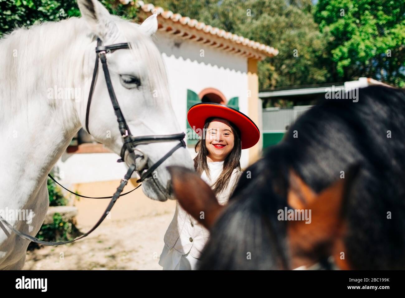 Adolescent avec syndrome de Down portant un chapeau rouge avec deux chevaux Banque D'Images