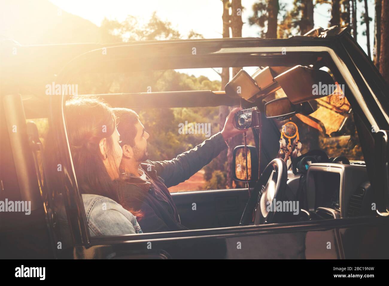 Jeune couple avec tablette numérique appareil photo prenant selfie en jeep dans les bois ensoleillés Banque D'Images