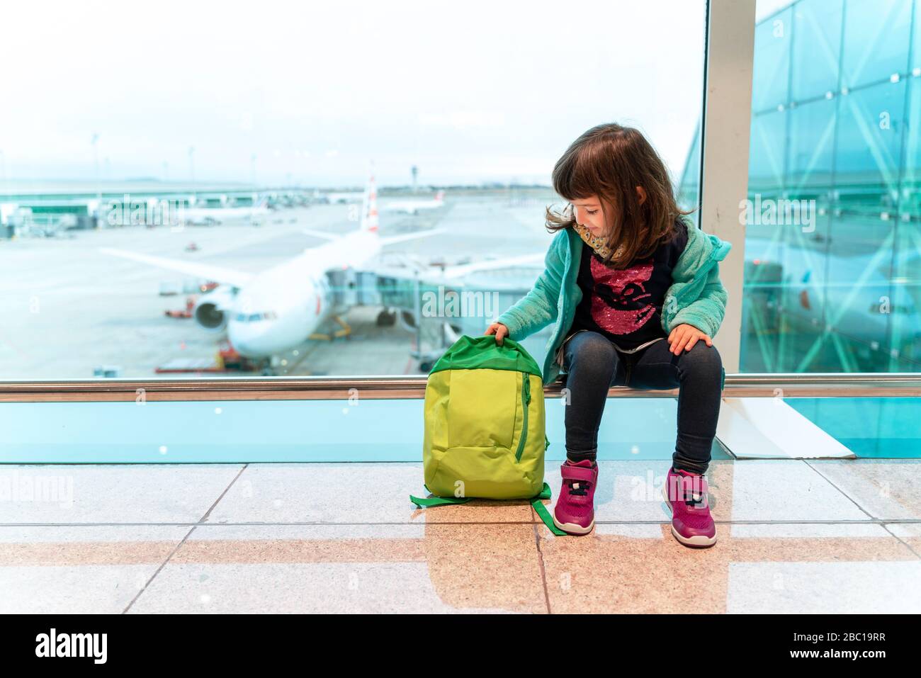 Fille avec sac à dos assis à l'aéroport en face d'un avion Banque D'Images