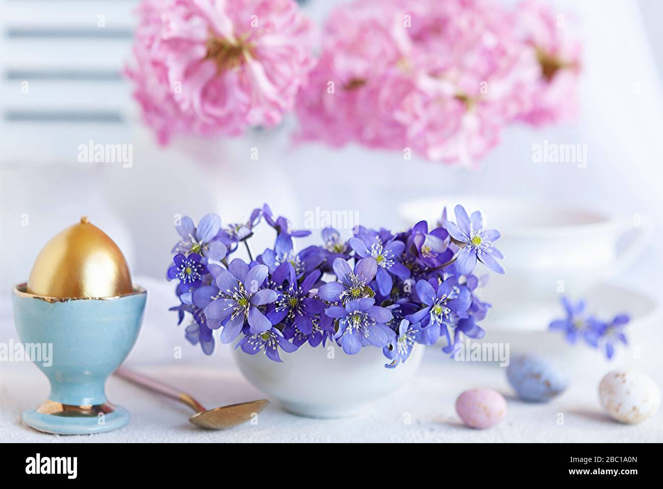 Bouquet frais de fleurs printanières délicates liverwort Hepatica Nobilis et un œuf doré dans un stand d'œufs - petit déjeuner pour Pâques matin Banque D'Images