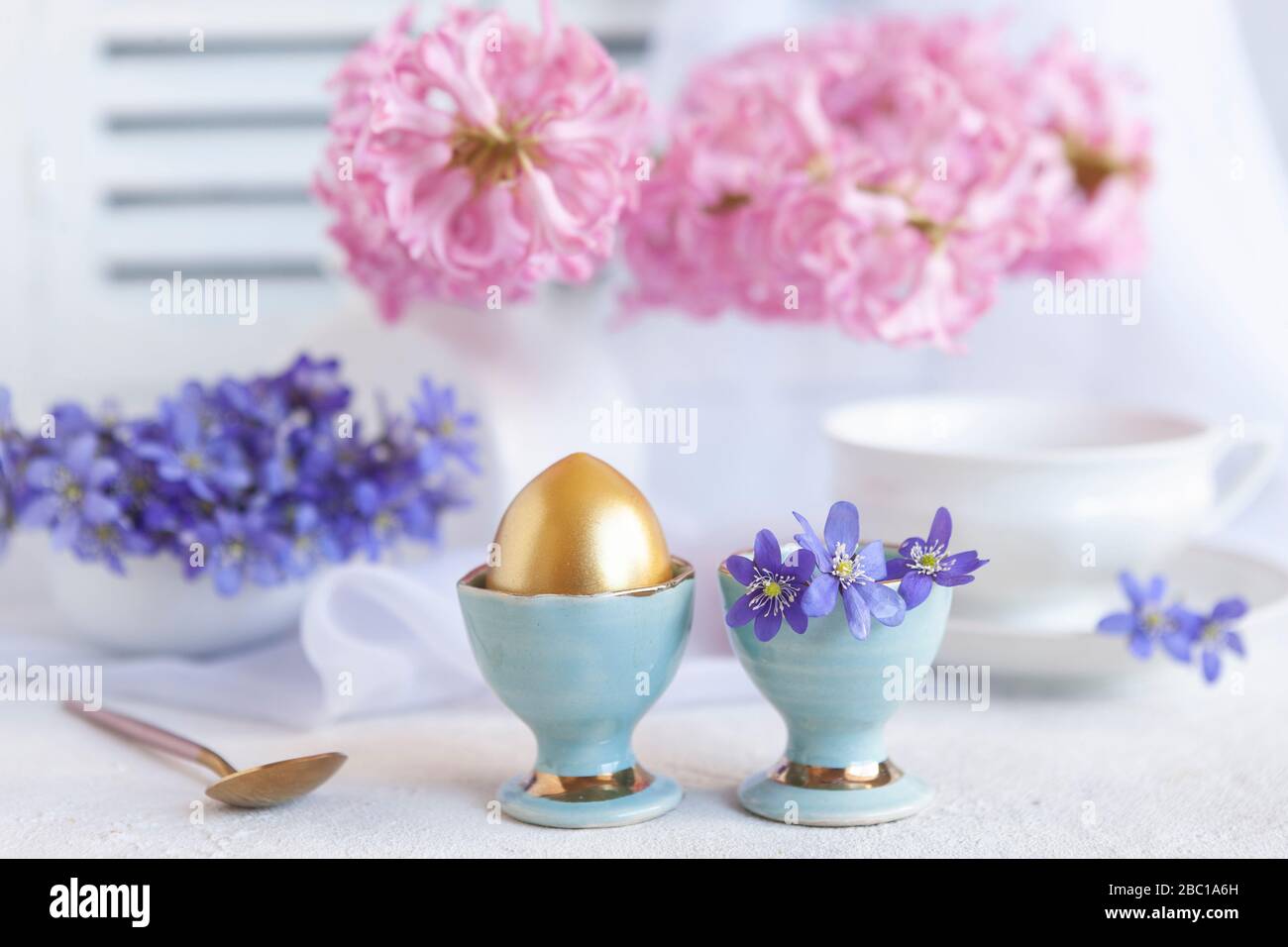 Bouquet frais de fleurs printanières délicates liverwort Hepatica Nobilis et un œuf doré dans un stand d'œufs - petit déjeuner pour Pâques matin Banque D'Images