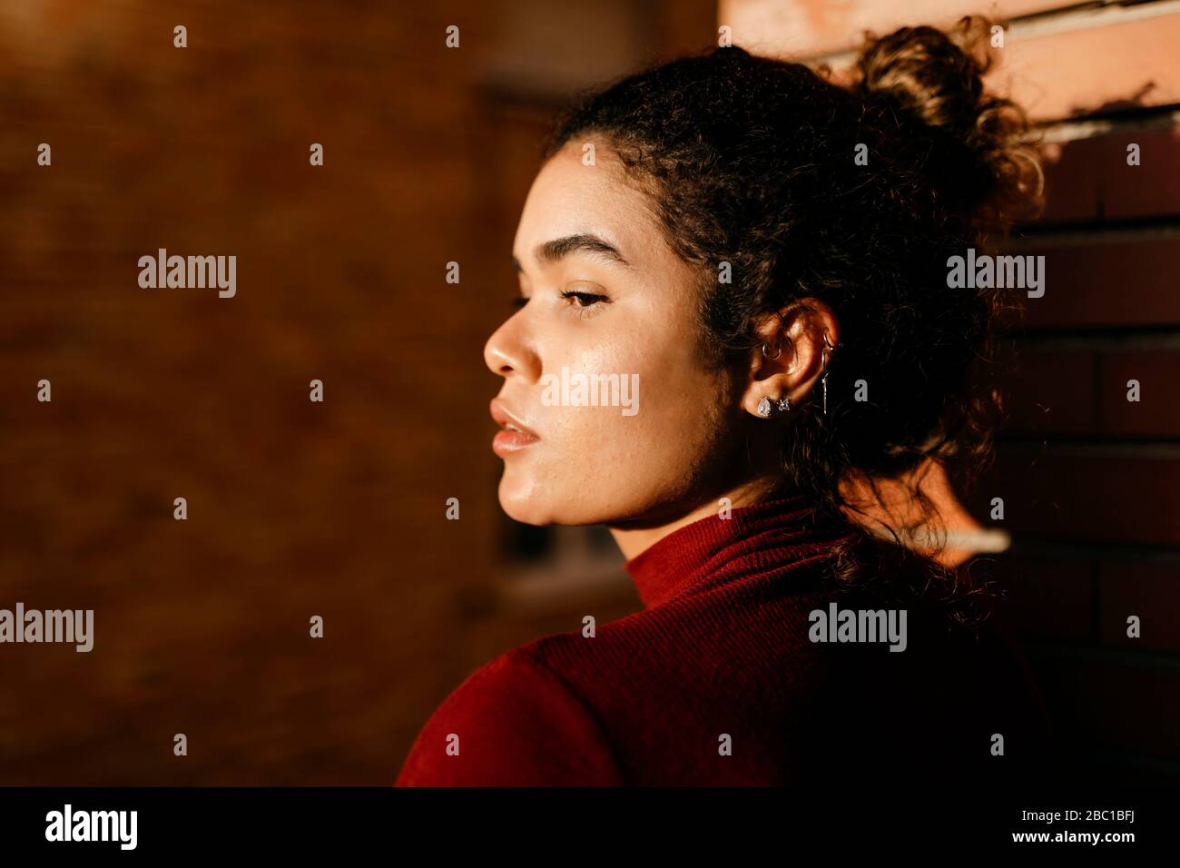 Portrait de la jeune femme portant un pull à col roulé rouge, lumière du soleil sur son visage Banque D'Images