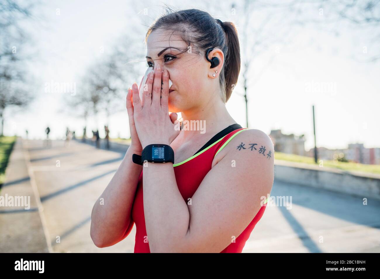 Jeune femme sportive avec écouteurs sans fil soufflant son nez Banque D'Images