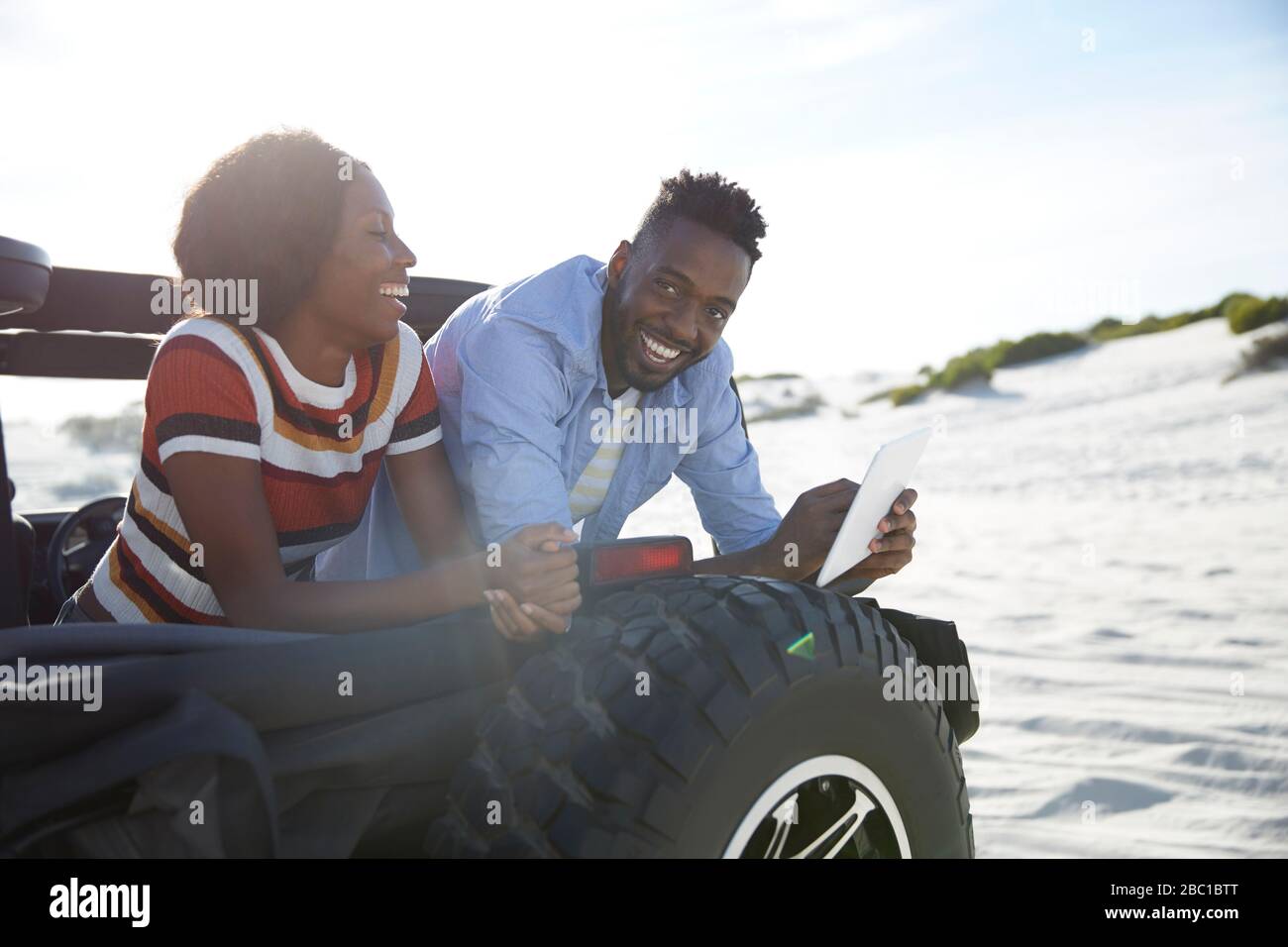 Jeune couple souriant utilisant une tablette numérique en jeep sur la plage ensoleillée Banque D'Images