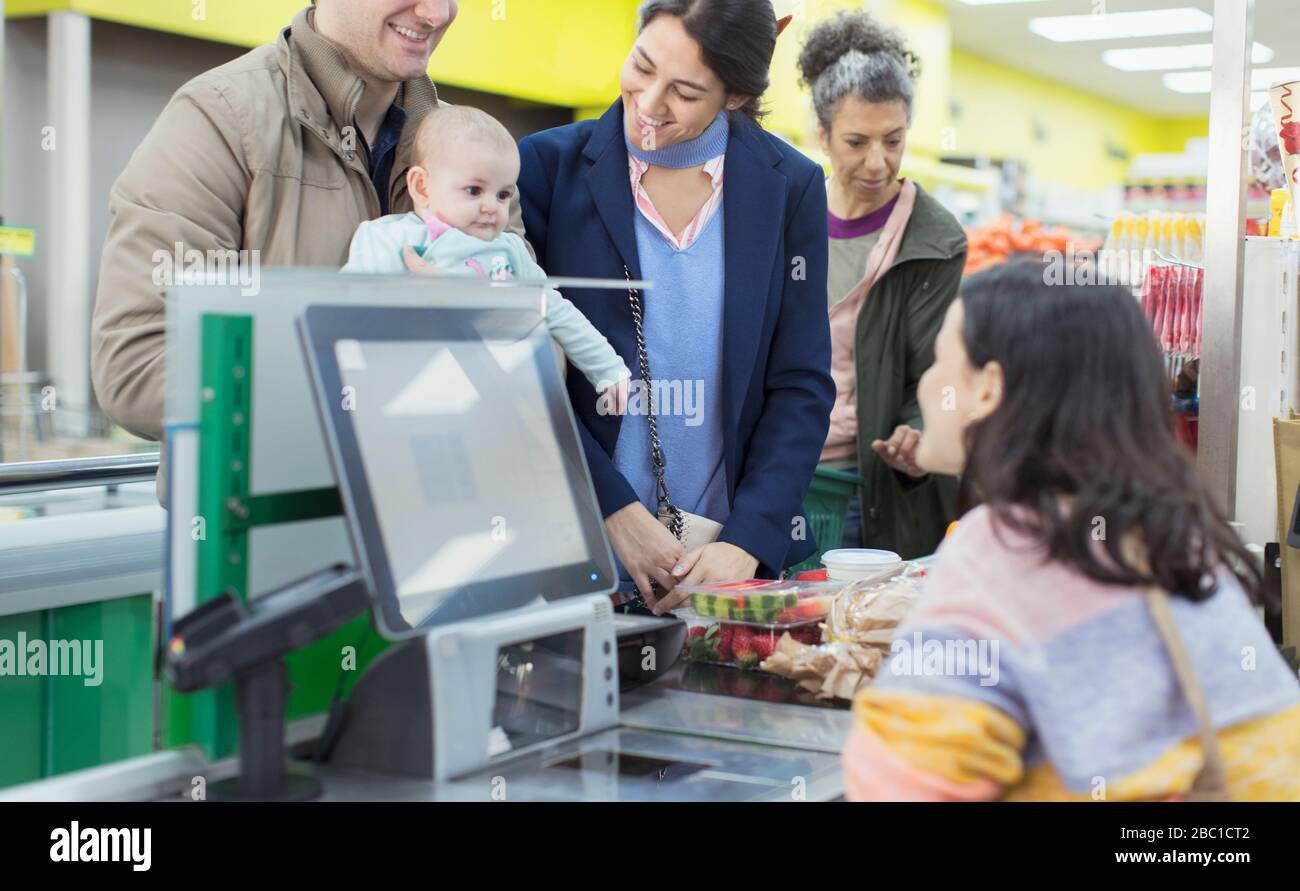 Un caissier sympathique qui parle avec un couple avec un bébé au moment du contrôle au supermarché Banque D'Images