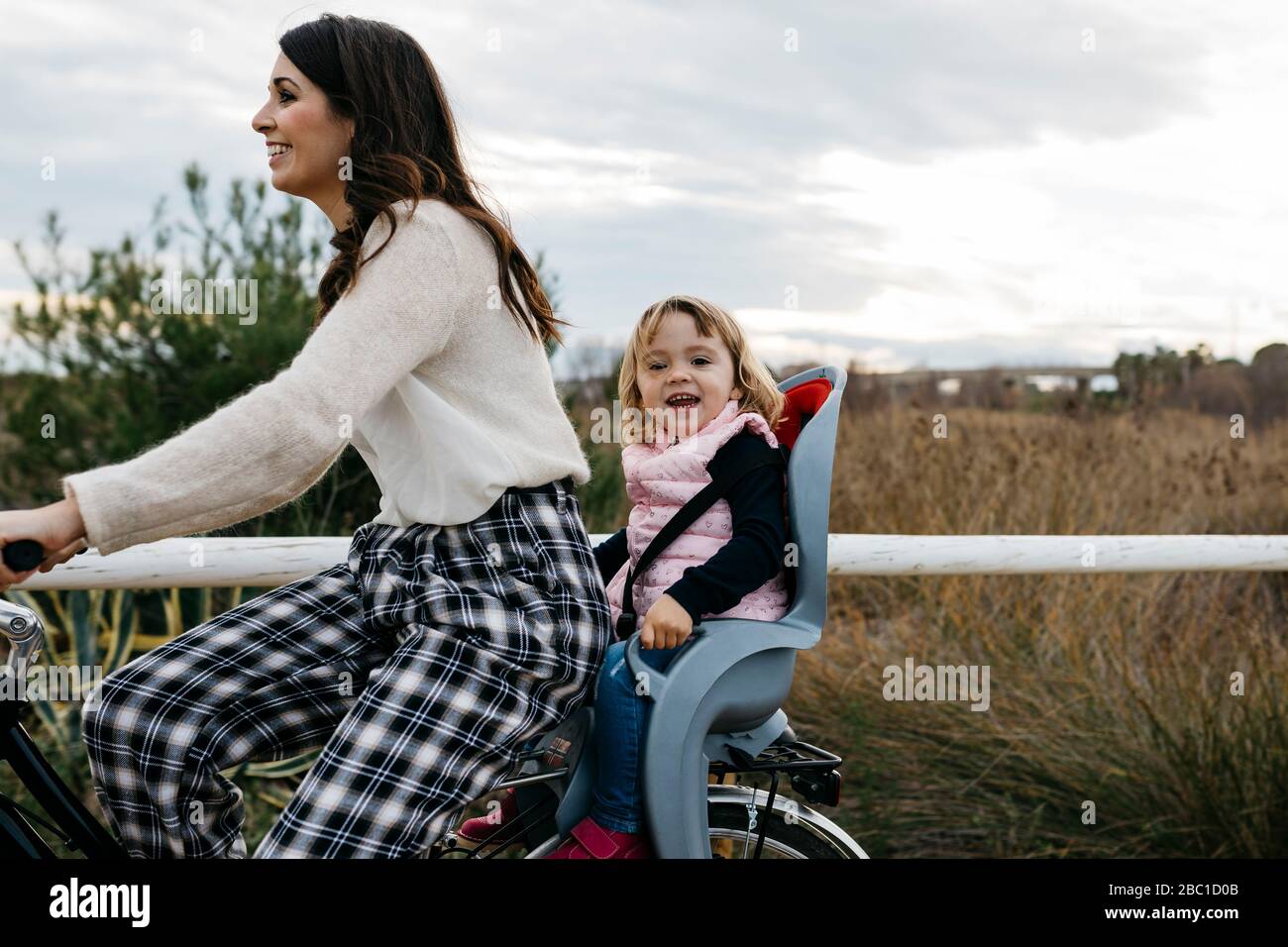 Femme à vélo dans la campagne avec une heureuse fille dans le siège de l'enfant Banque D'Images