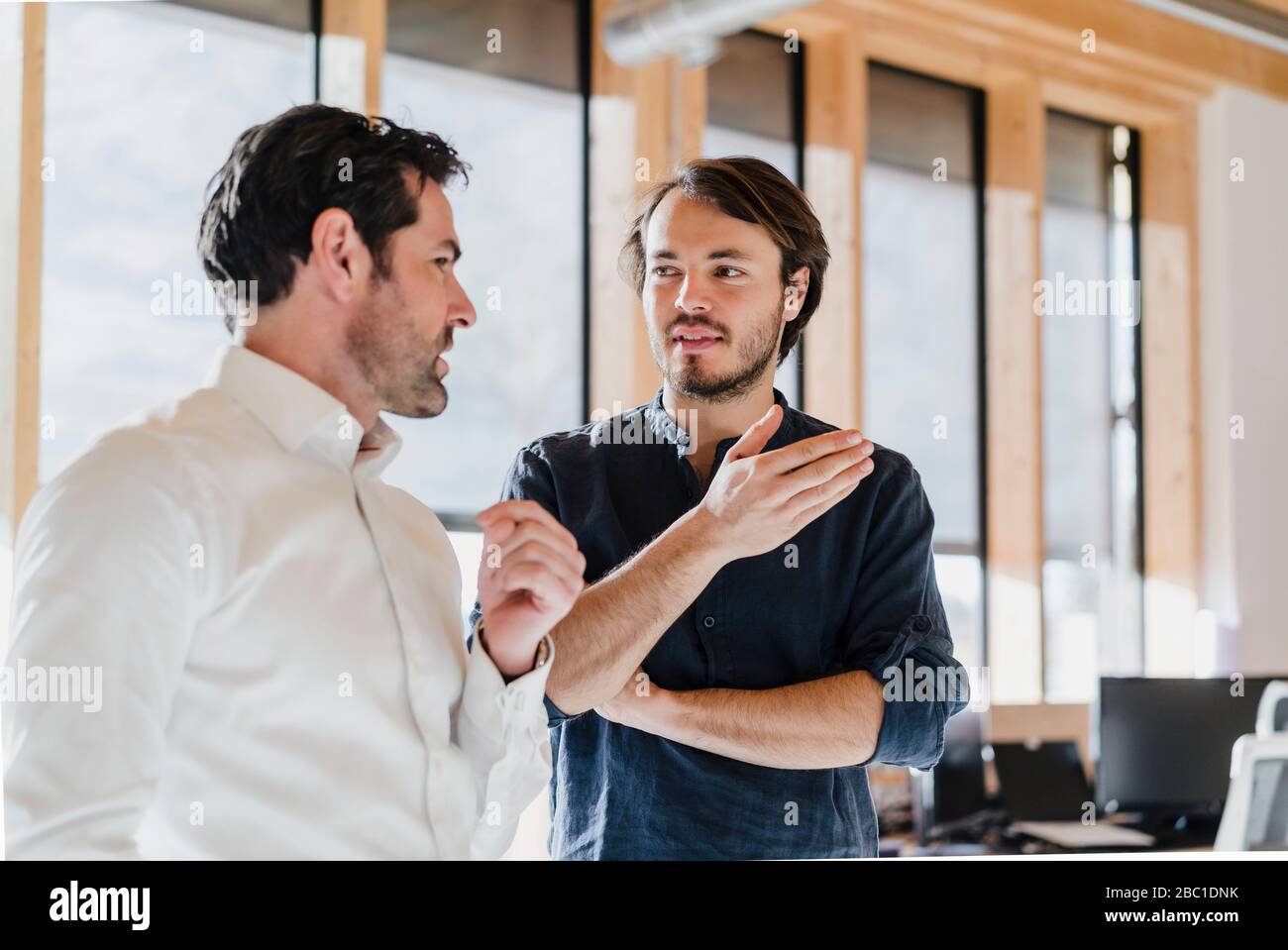 Deux hommes d'affaires parlent dans un bureau en bois à plan ouvert Banque D'Images