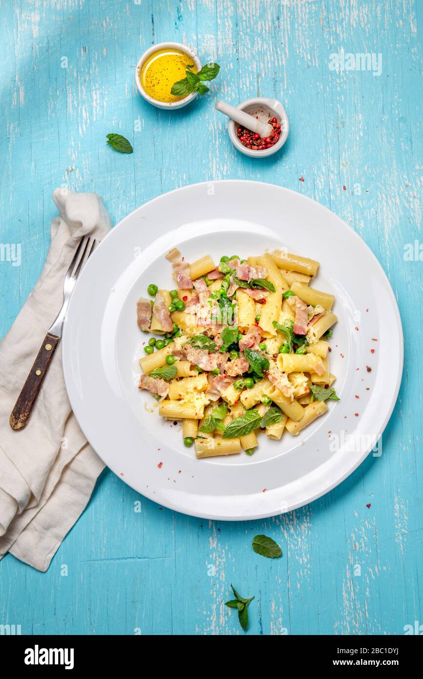 Recette italienne Pasta tortilloni avec pois verts, feuilles de menthe, cheece, bacon fumé et fromage. Vue de dessus, arrière-plan bleu. Banque D'Images