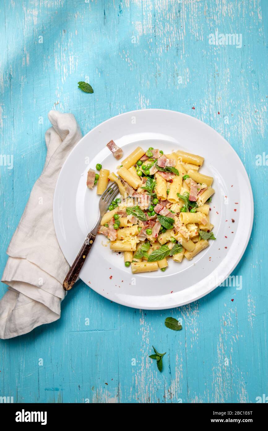 Recette italienne Pasta tortilloni avec pois verts, feuilles de menthe, cheece, bacon fumé et fromage. Vue de dessus, arrière-plan bleu. Banque D'Images