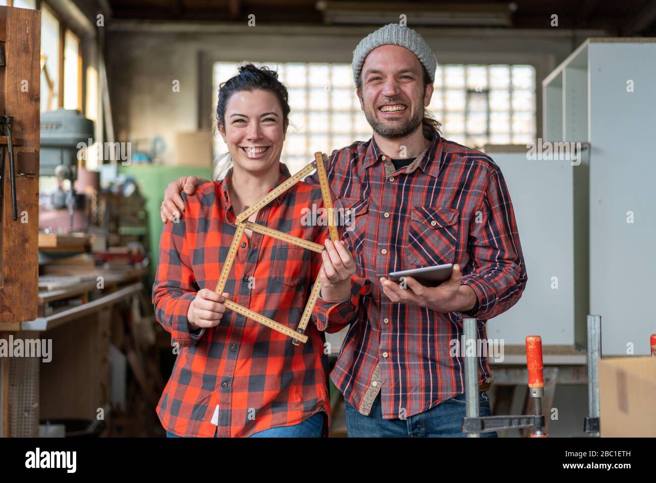 Portrait de l'artisan heureux et de l'artisan tenant tablette et yardstick dans leur atelier Banque D'Images
