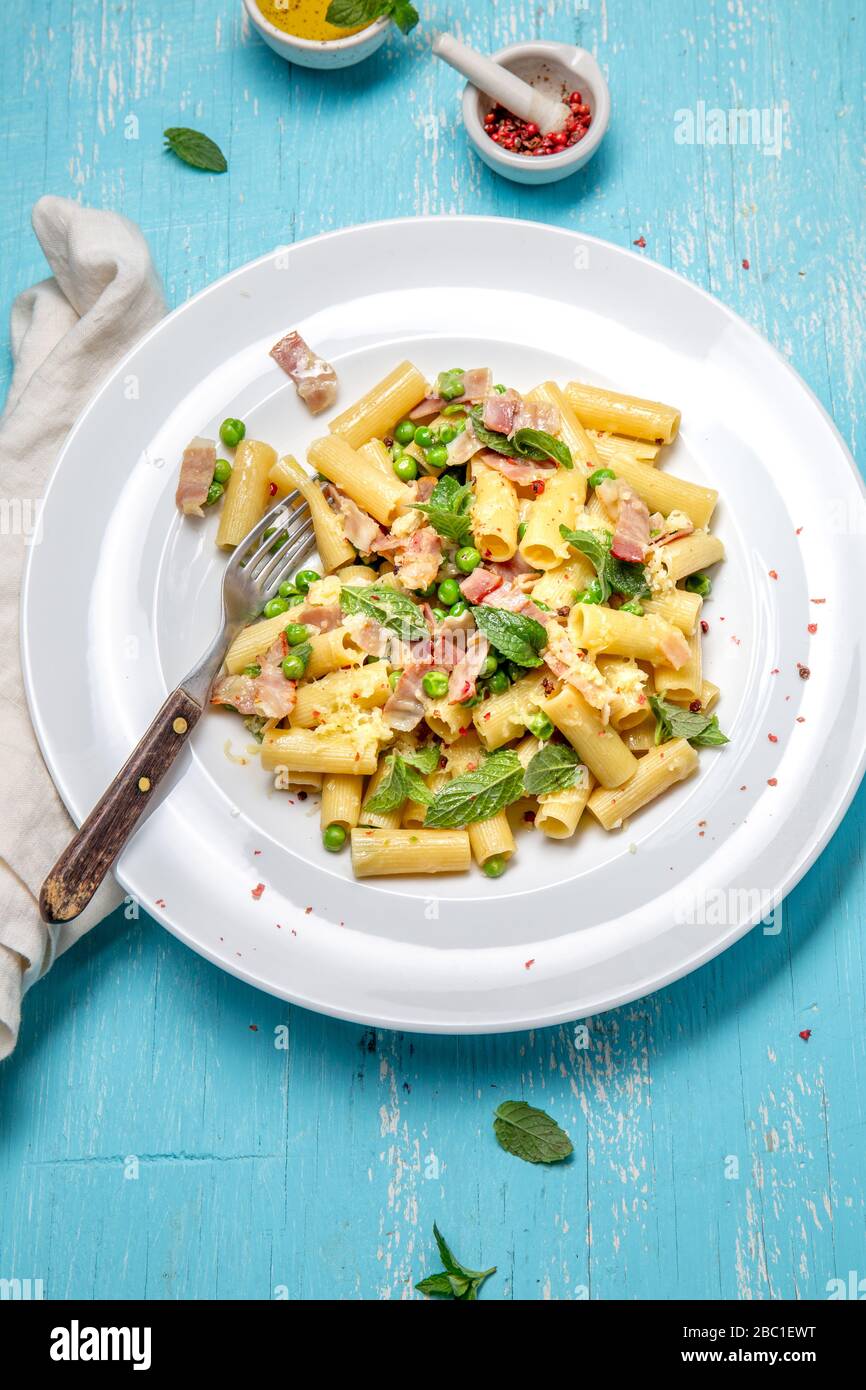 Recette italienne Pasta tortilloni avec pois verts, feuilles de menthe, cheece, bacon fumé et fromage. Vue de dessus, arrière-plan bleu. Banque D'Images
