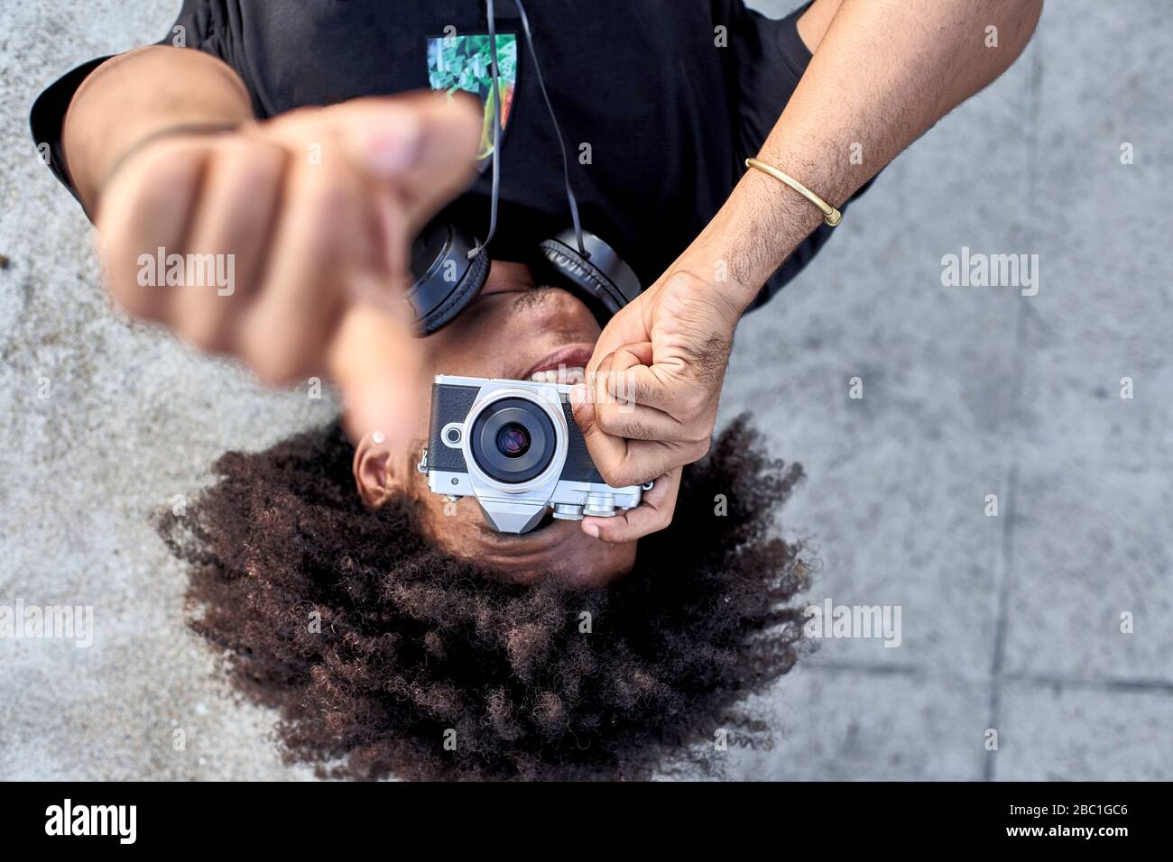 Jeune homme posé sur le mur et prenant des photos avec son appareil photo et pointant avec son doigt Banque D'Images