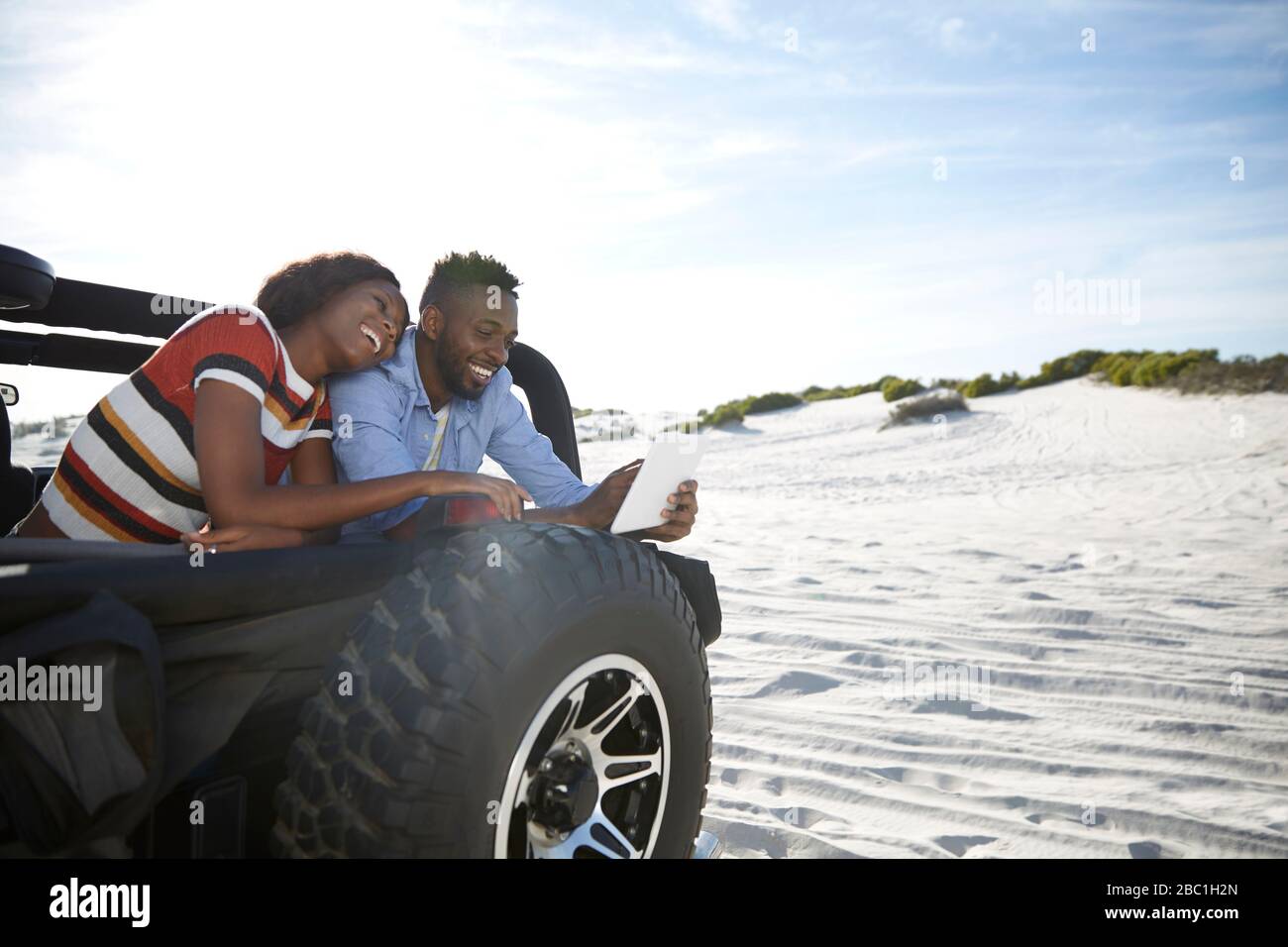 Jeune couple utilisant une tablette numérique en jeep sur la plage ensoleillée, en profitant de la route Banque D'Images