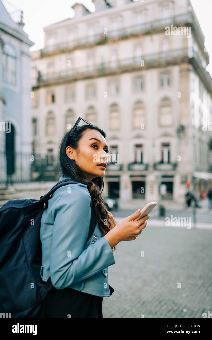 Portrait de la jeune femme avec sac à dos et smartphone regardant quelque chose, Lisbonne, Portugal Banque D'Images