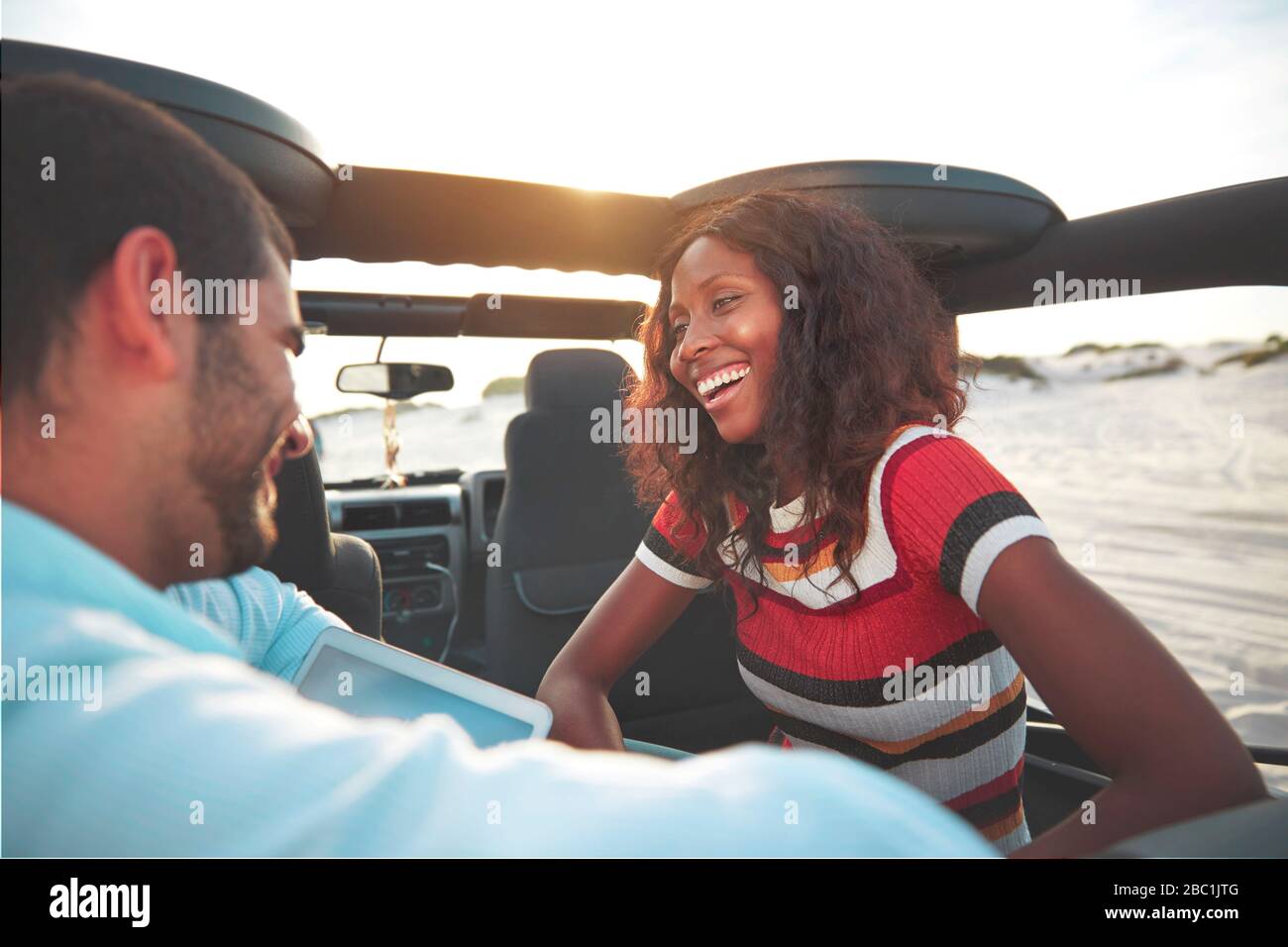 Jeune couple souriant en train de monter sur place à l'arrière de la jeep sur la plage, en profitant d'un voyage sur la route Banque D'Images