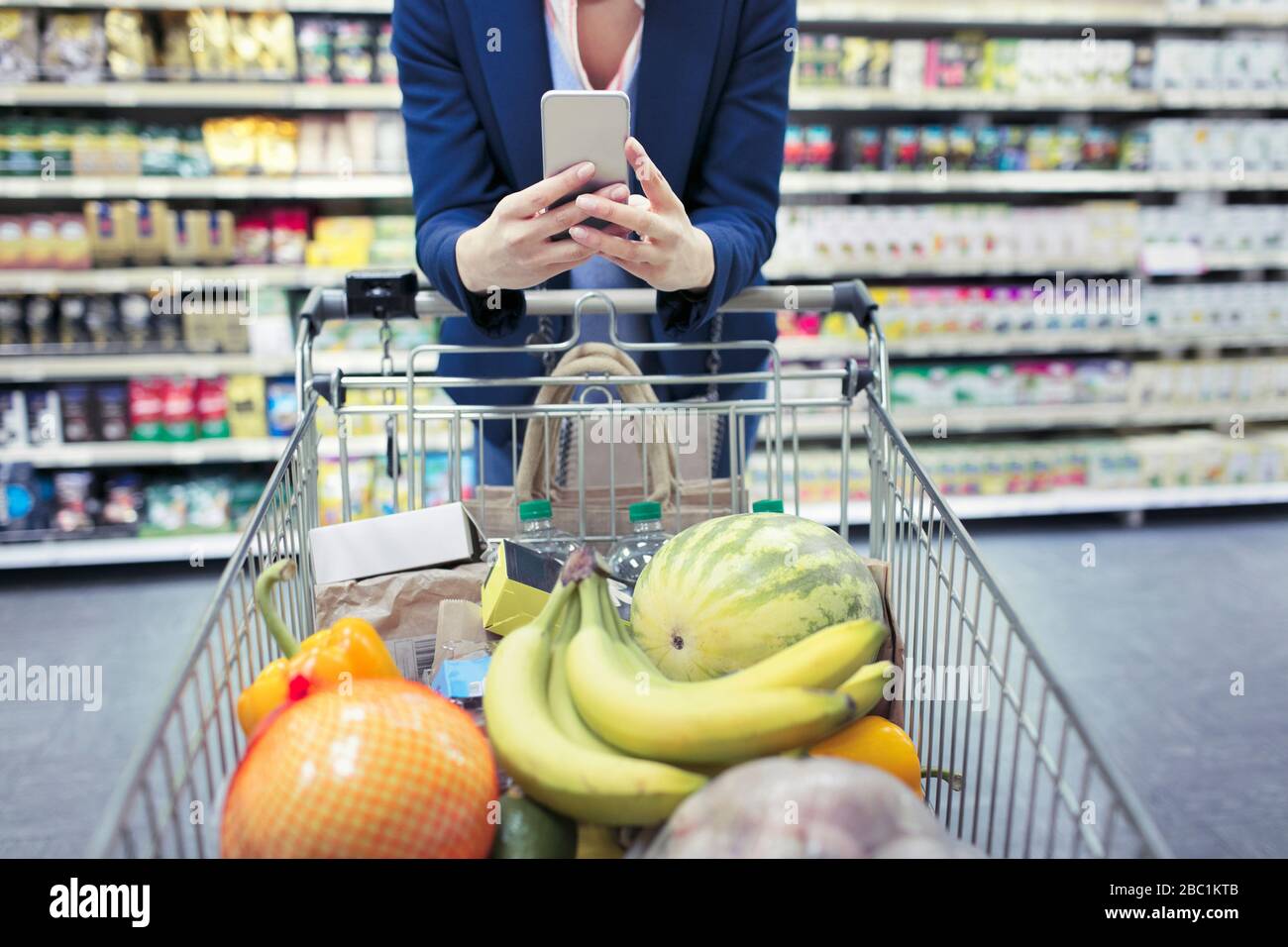 Femme avec smartphone poussant panier dans le supermarché Banque D'Images