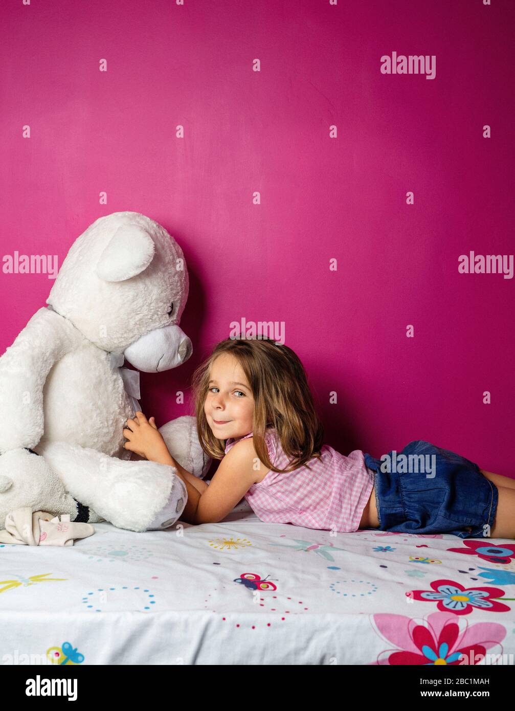 Portrait de la petite fille avec grand ours en peluche devant le mur rose Banque D'Images
