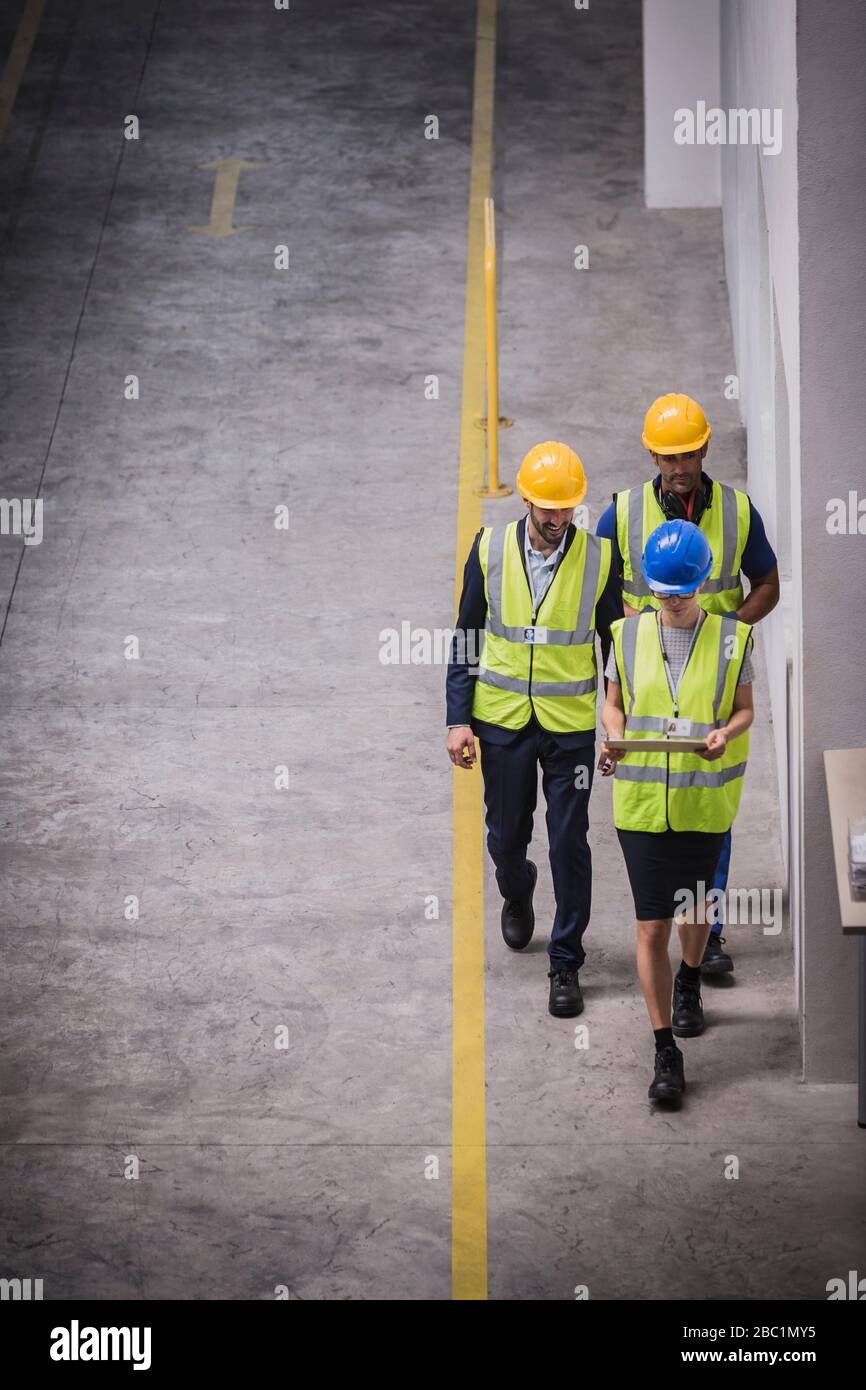 Superviseur et travailleurs avec tablette numérique marchant en usine Banque D'Images