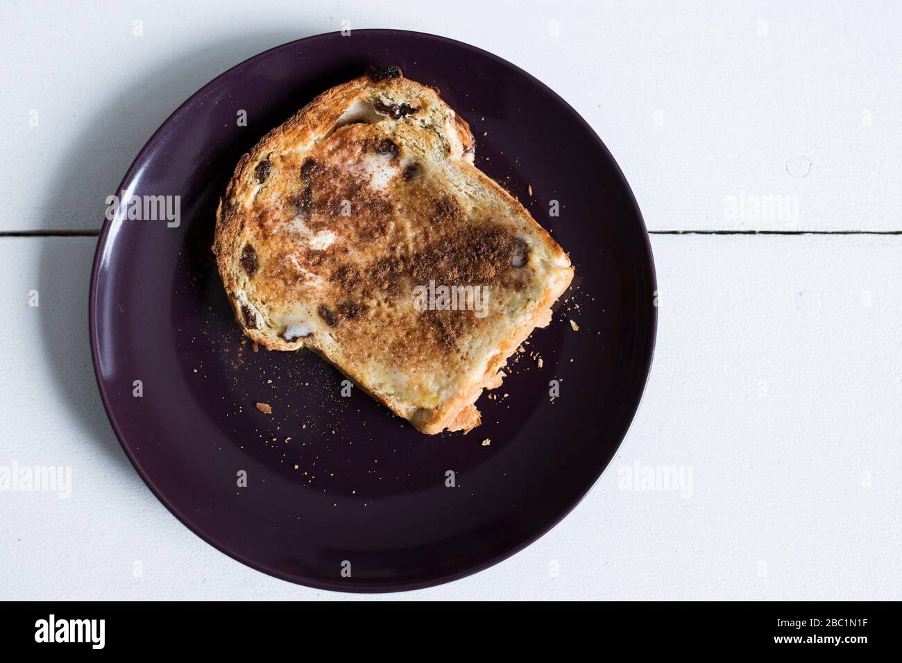 Un morceau de pain grillé au raisin avec cannelle et sucre est prêt pour le petit-déjeuner sur une plaque violette et une table blanche. Banque D'Images