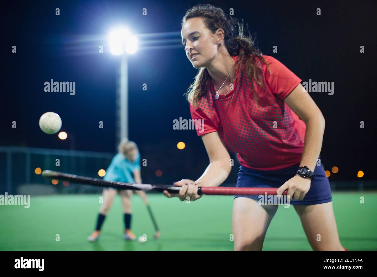 Jeune joueur de hockey sur gazon féminin qui rebondit la balle sur le bâton de hockey, pratique sur le terrain la nuit Banque D'Images