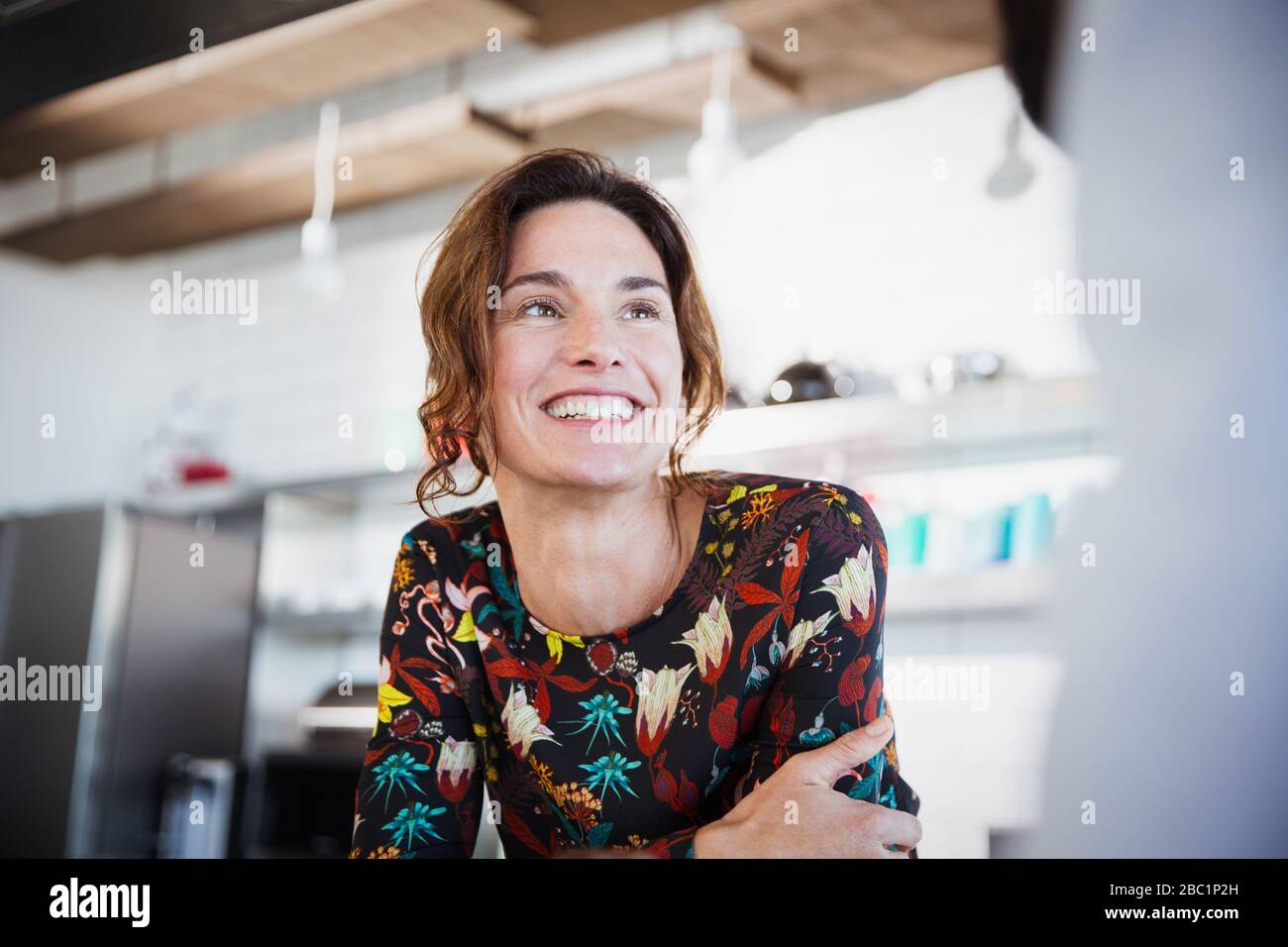 Femme brunette souriante écoutant, regardant loin dans la cuisine Banque D'Images