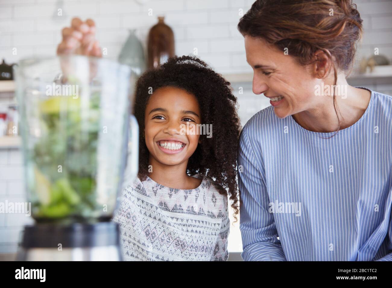 La mère et la fille font un smoothie vert sain dans le mixeur dans la cuisine Banque D'Images