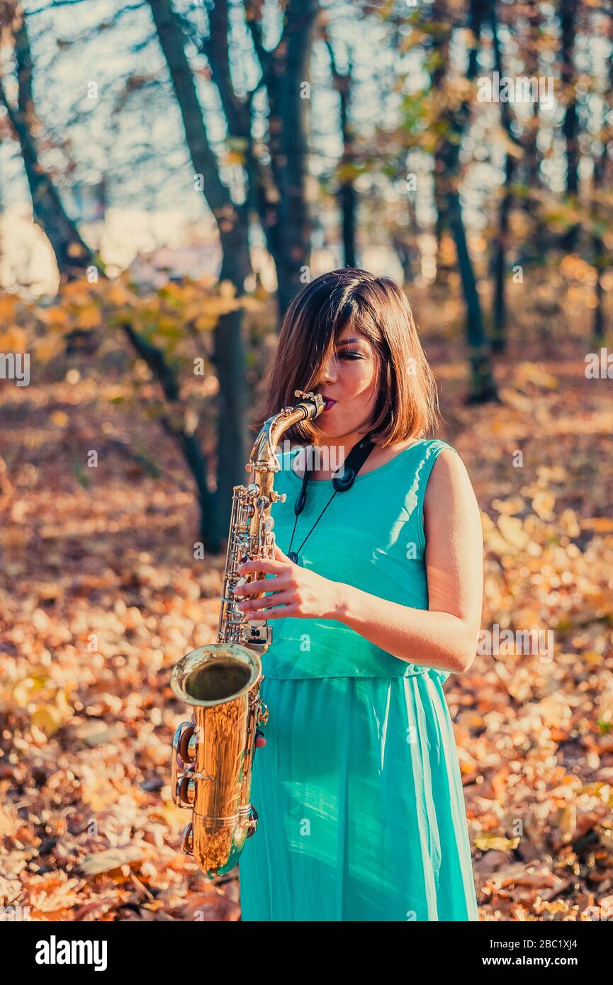 une jeune femme divine à poil sombre, vêtue d'une longue robe bleue, joue  le saxophone alto sur le fond du feuillage tombé des arbres dans un autum  jaune Photo Stock - Alamy