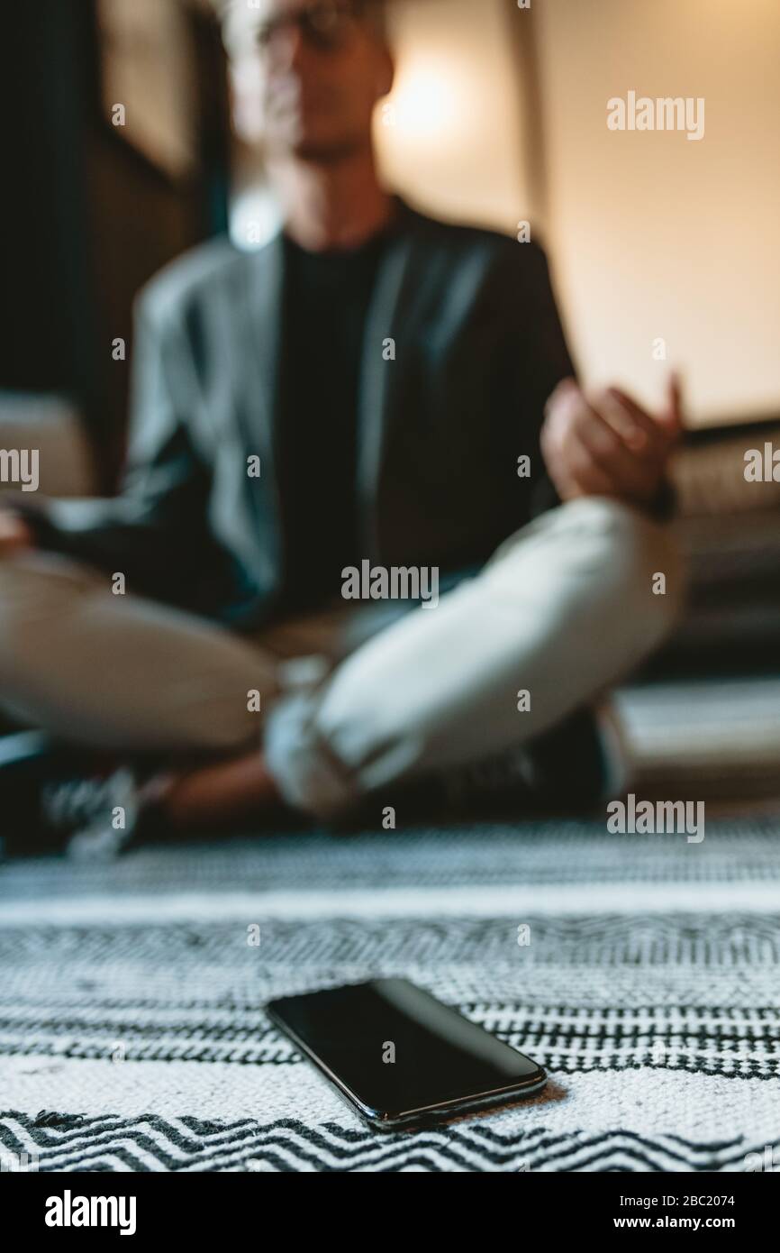 Plan à angle bas d'un homme d'affaires adulte moyen faisant de la méditation de yoga avec son téléphone portable devant. professionnel des affaires méditant dans la pose de yoga en offic Banque D'Images Plan à angle bas d'un homme d'affaires adulte moyen faisant de la méditation de yoga avec son téléphone portable devant. professionnel des affaires méditant dans la pose de yoga en offic Banque D'Images