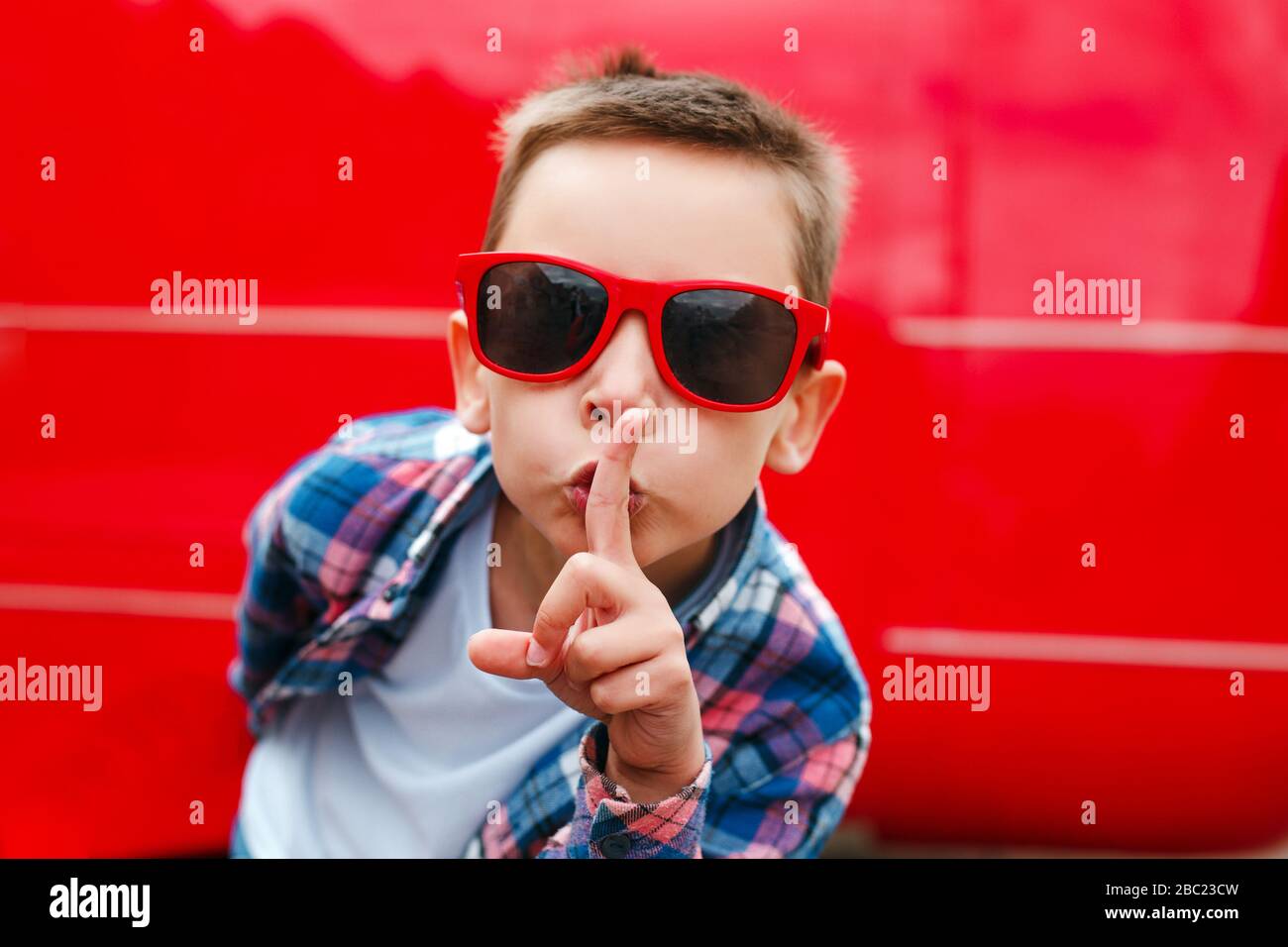 Garçon dans des lunettes de soleil rouges avec le doigt sur les lèvres  faisant un geste silencieux en ville Photo Stock - Alamy