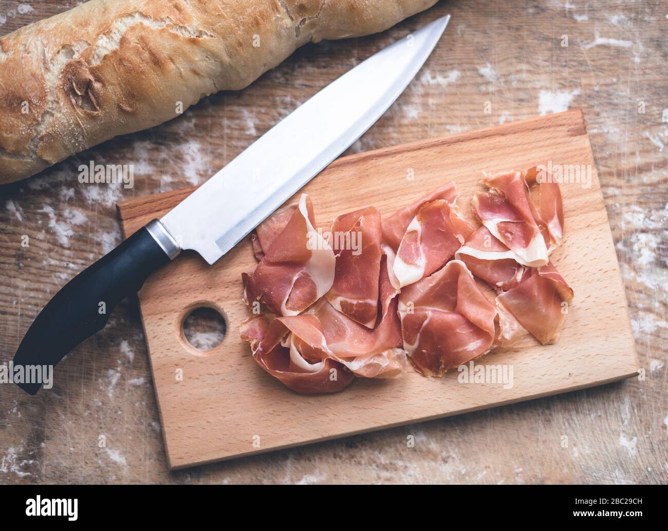 Prosciutto, baguette et couteau espagnols sur la table. Table en bois dégoûtée avec farine Banque D'Images