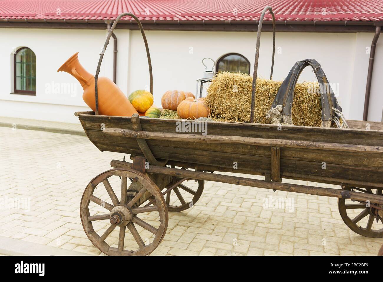 Pichet en terre cuite et citrouilles orange sur un chariot avec roues en bois. Cour de ferme Banque D'Images