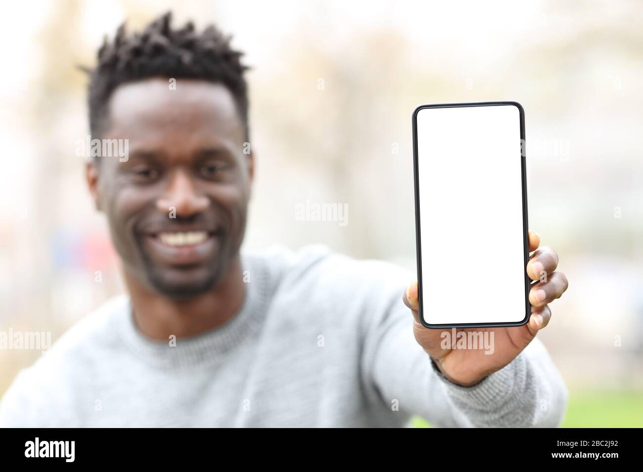 Vue de face d'un homme noir heureux montrant l'écran du téléphone se moquer dans un parc Banque D'Images