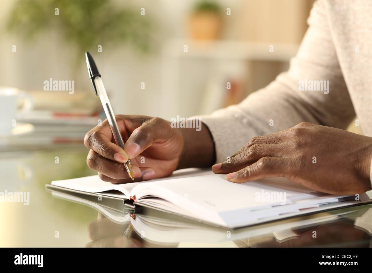 Gros plan sur un homme noir mains écrire rappel sur papier agenda sur un bureau à la maison Banque D'Images