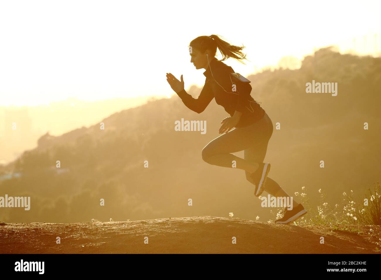 Vue latérale portraif d'une femme de coureur qui monte rapidement un mountaing au coucher du soleil Banque D'Images