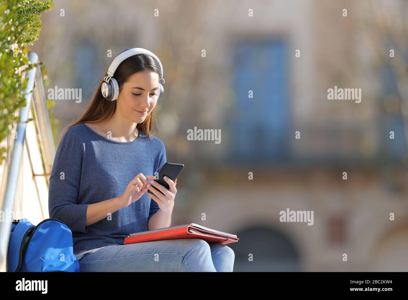 Les étudiants portent un casque pour écouter de la musique à l'aide d'un smartphone assis à l'extérieur dans un campus universitaire Banque D'Images