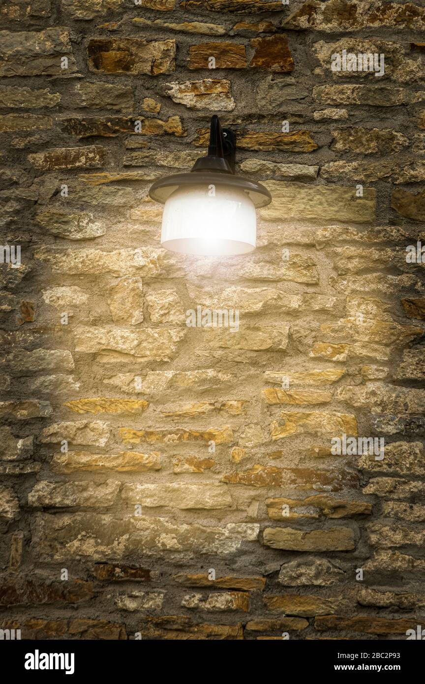 Vieux mur de ville bien gardé en pierre naturelle avec des pierres plates et larges de la lumière jaunâtre à la rouille brun avec une belle et brillante lampe d'extérieur vintage Banque D'Images